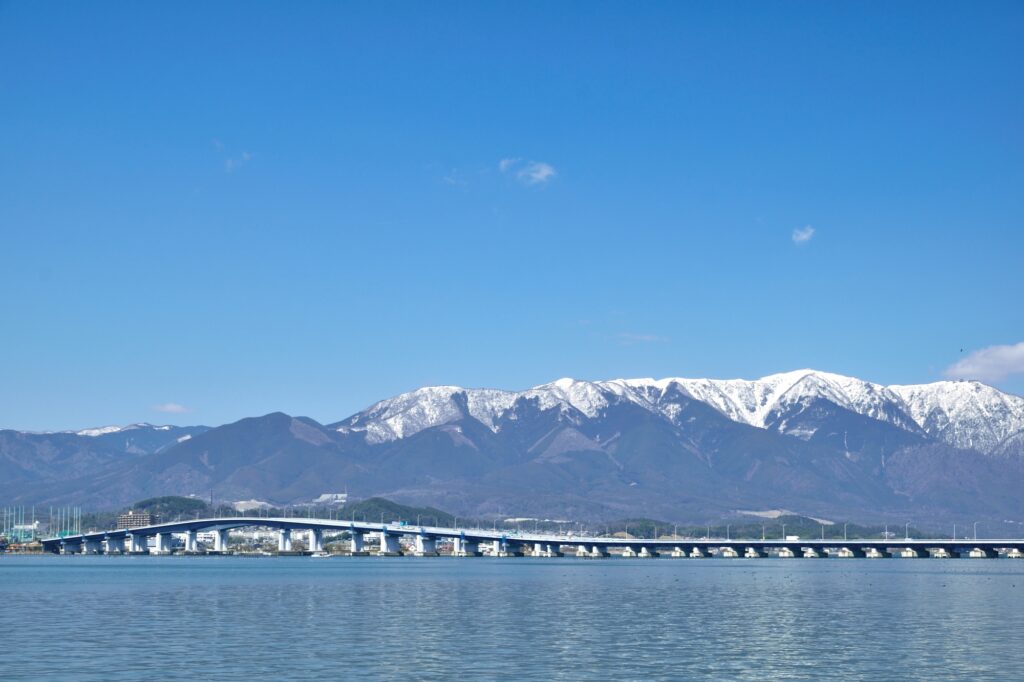 早春の琵琶湖を通る琵琶湖大橋と背景になる雪の比良山